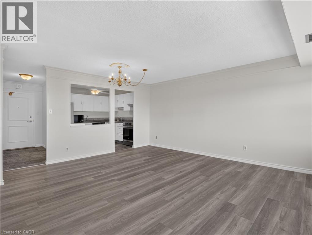 Spacious living area featuring wood-finish flooring, a decorative chandelier, and an open pass-through to the kitchen with white cabinetry - 7 Gale Crescent Unit# 1107, St. Catharines, ON