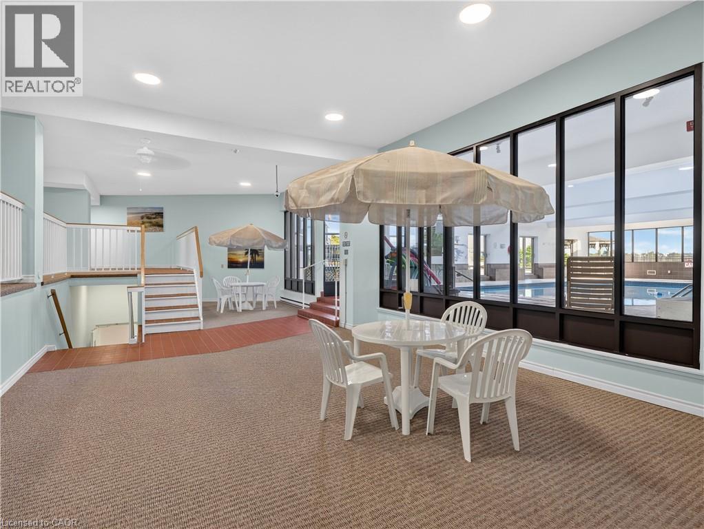 Indoor recreational area featuring large windows, a staircase with white railings, and a pool visible beyond the windows - 7 Gale Crescent Unit# 1107, St. Catharines, ON