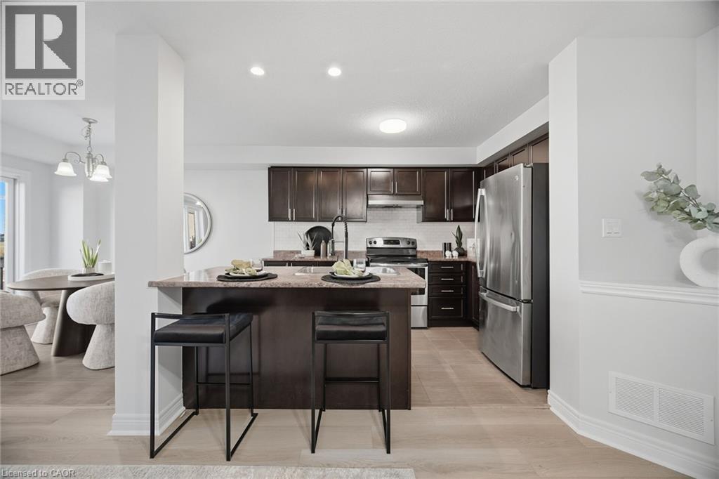 Kitchen featuring dark wood-finish cabinetry, stainless steel appliances, a light-colored tile backsplash, a peninsula with a stone countertop, and recessed lighting - 98 Bloom Crescent, Stoney Creek, ON