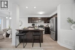 Kitchen featuring dark wood-finish cabinetry, stainless steel appliances, a light-colored tile backsplash, a peninsula with a stone countertop, and recessed lighting -