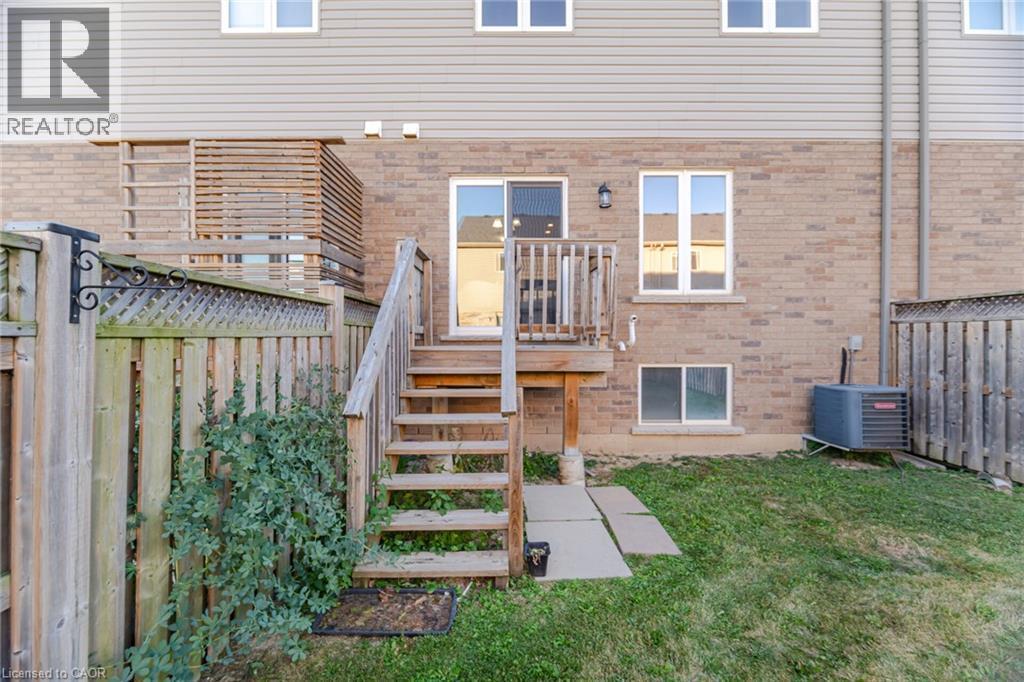 Brick and siding exterior featuring a wooden deck with stairs, a sliding glass door, and a ground-level window - 98 Bloom Crescent, Stoney Creek, ON