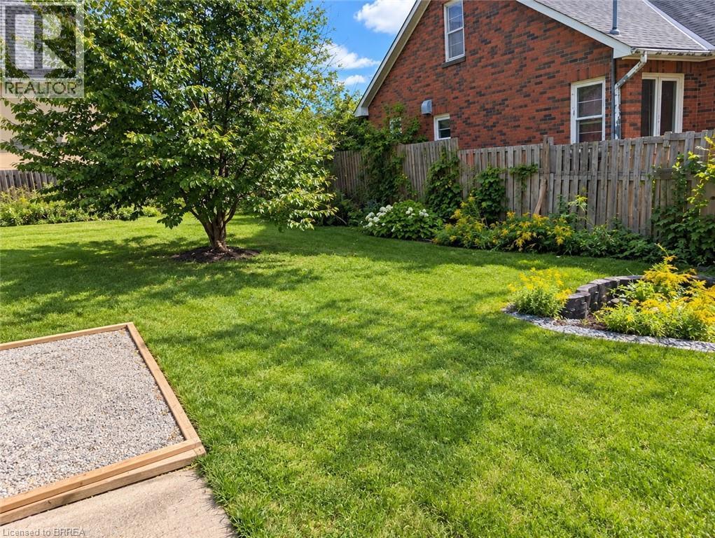 Expansive green lawn featuring a mature shade tree, a gravel patio area, and a brick house exterior - 106 Catharine Avenue, Brantford, ON