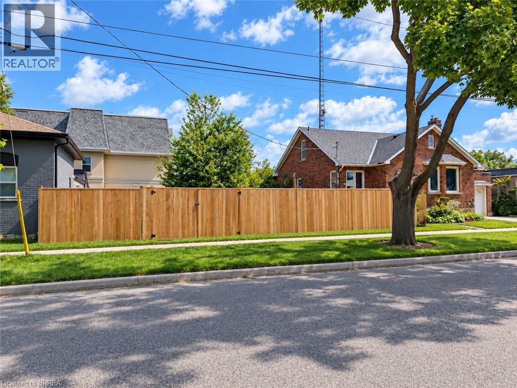 Brick exterior with a dark shingle roof, mature front yard tree, and a newly installed wood privacy fence - 106 Catharine Avenue, Brantford, ON