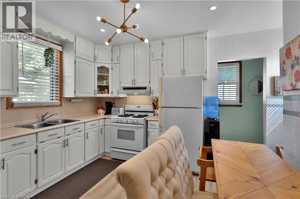 White cabinetry with brushed nickel hardware, stainless steel double basin sink, neutral countertops, gas range, and a contemporary brass chandelier - 7 Halls Avenue, Brantford, ON