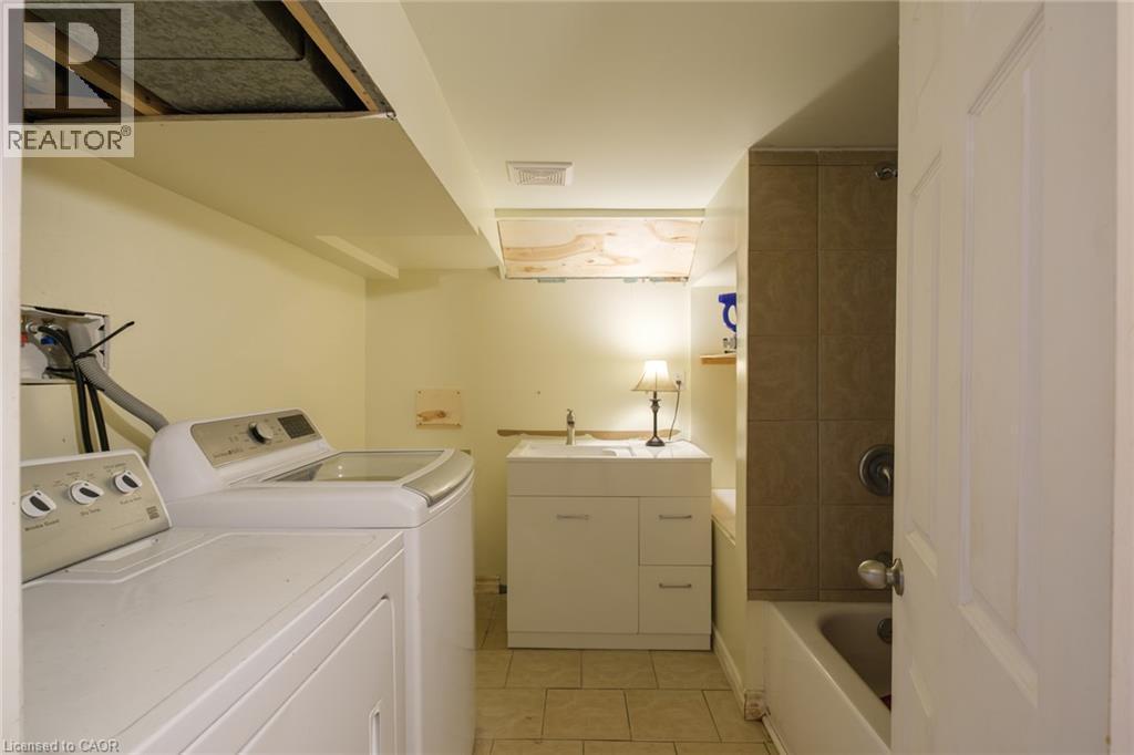 Laundry area with tiled flooring, utility sink with base cabinetry, and a full bathtub with tiled surround - 78 Oak Street, Simcoe, ON