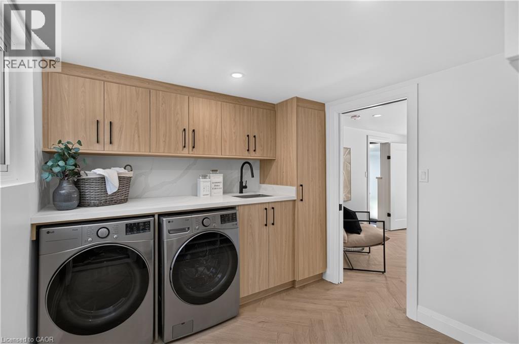 Integrated laundry area featuring wood-finish cabinetry, a white countertop, a black faucet, and a herringbone-patterned floor - 3028 Eva Drive, Burlington, ON