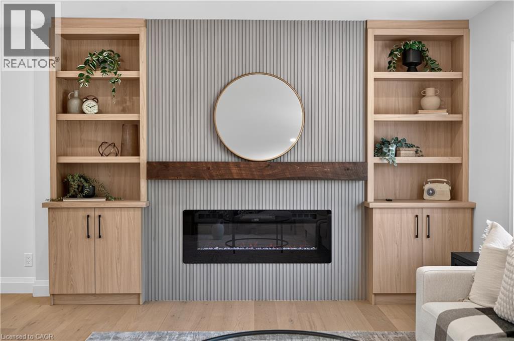 Built-in shelving with lower cabinetry, reeded accent wall, wood-finish mantel, and an electric fireplace - 3028 Eva Drive, Burlington, ON