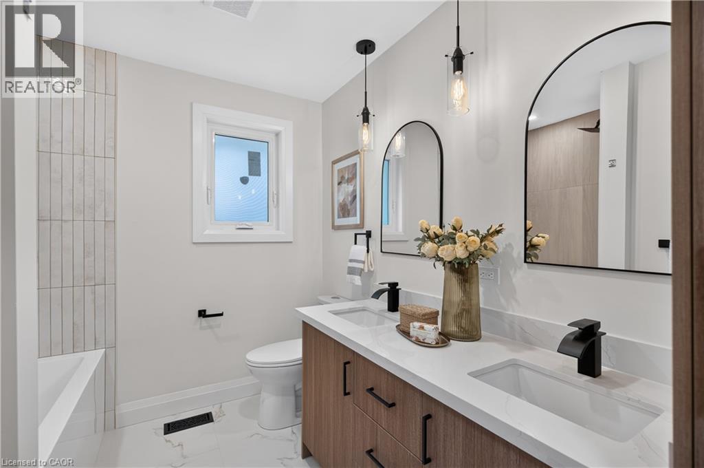 Dual arched mirrors, dual undermount sinks, wood-finish vanity, matte black fixtures, and vertical tile shower surround - 3028 Eva Drive, Burlington, ON