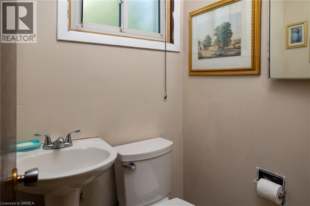 Pedestal sink with dual-handle chrome faucet, white commode, and a window with frosted glass - 52 Brier Park Road, Brantford, ON