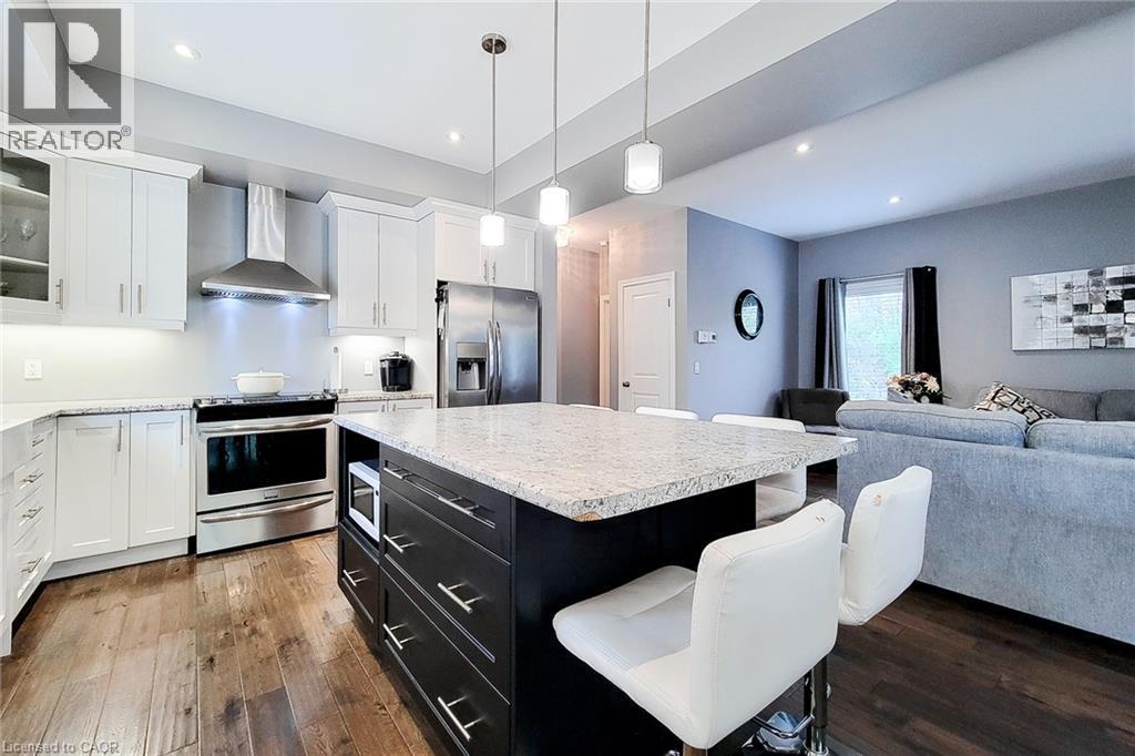 Kitchen featuring wood-finish flooring, white cabinetry, stainless steel appliances, and a central island with a light-toned countertop - 4274 Sixth Avenue, Niagara Falls, ON