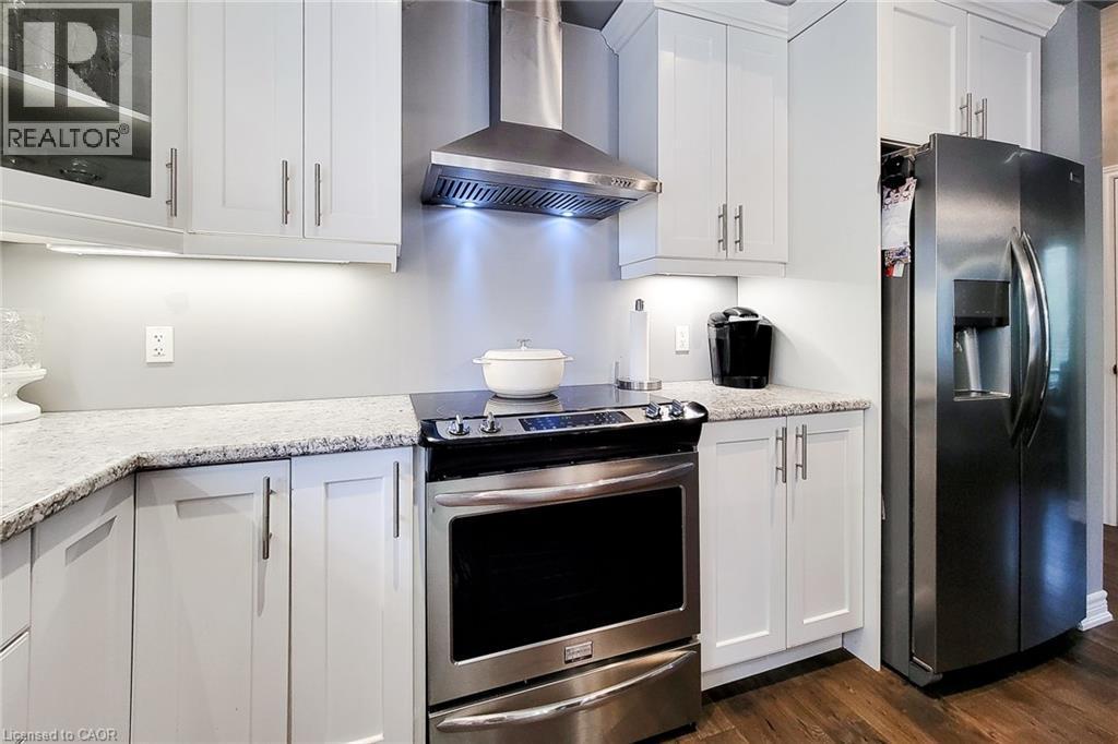 White cabinetry with brushed nickel hardware, stainless steel range with overhead ventilation, and a stainless steel refrigerator - 4274 Sixth Avenue, Niagara Falls, ON