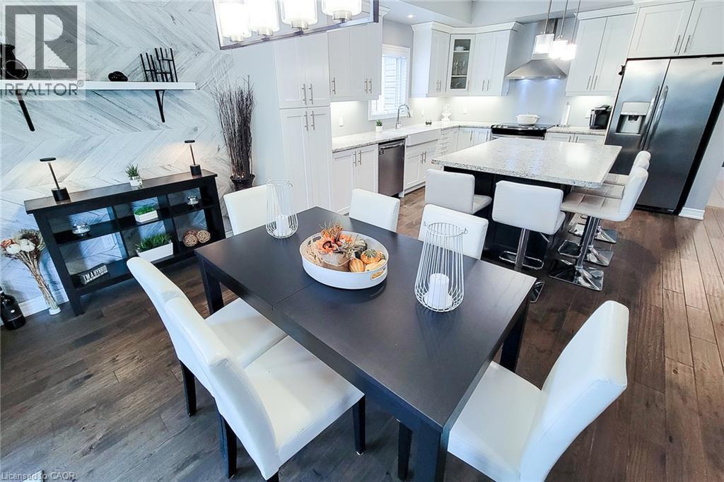 Open concept living area with wood-finish flooring, a contemporary kitchen featuring white cabinetry and stainless steel appliances, and a central island with bar seating - 4274 Sixth Avenue, Niagara Falls, ON