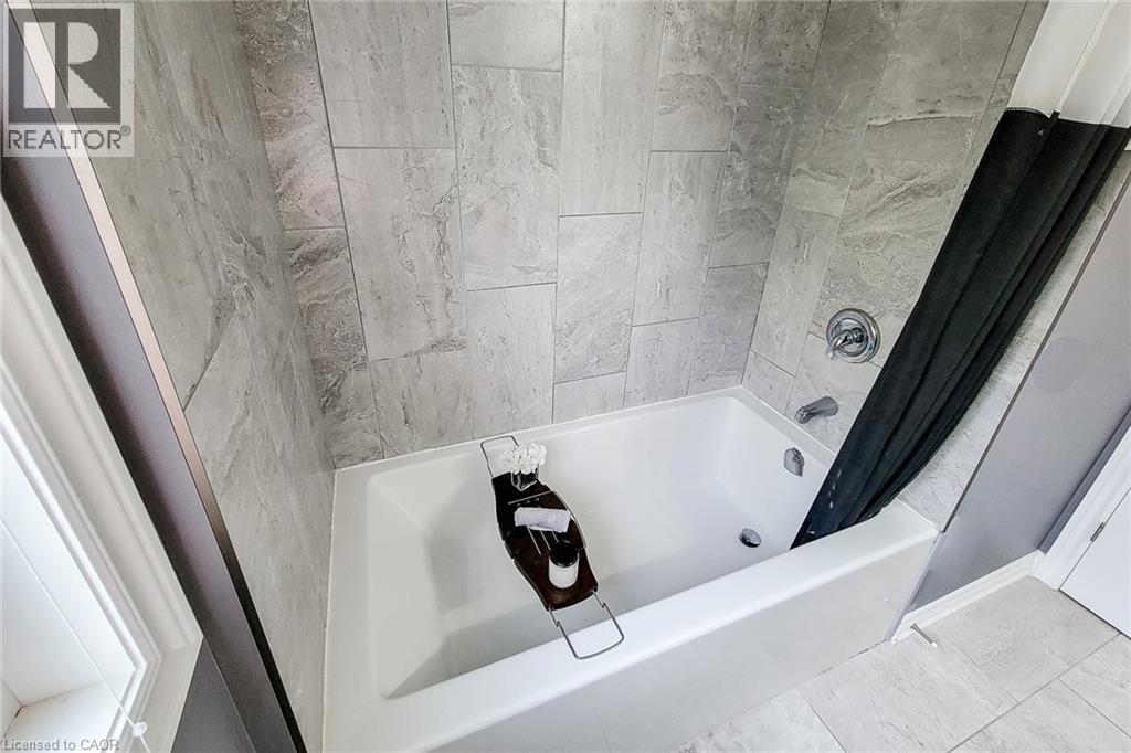 White soaking tub with chrome fixtures, surrounded by large format gray tile - 4274 Sixth Avenue, Niagara Falls, ON