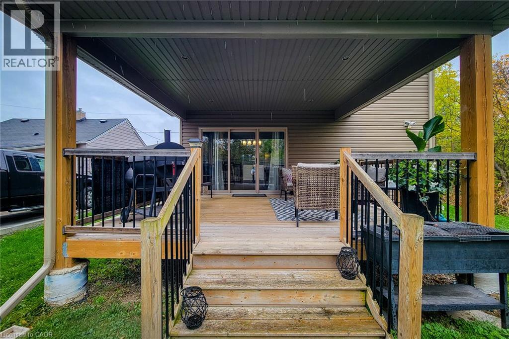 Covered deck with wood-finish stairs, durable railings, and sliding glass door access - 4274 Sixth Avenue, Niagara Falls, ON