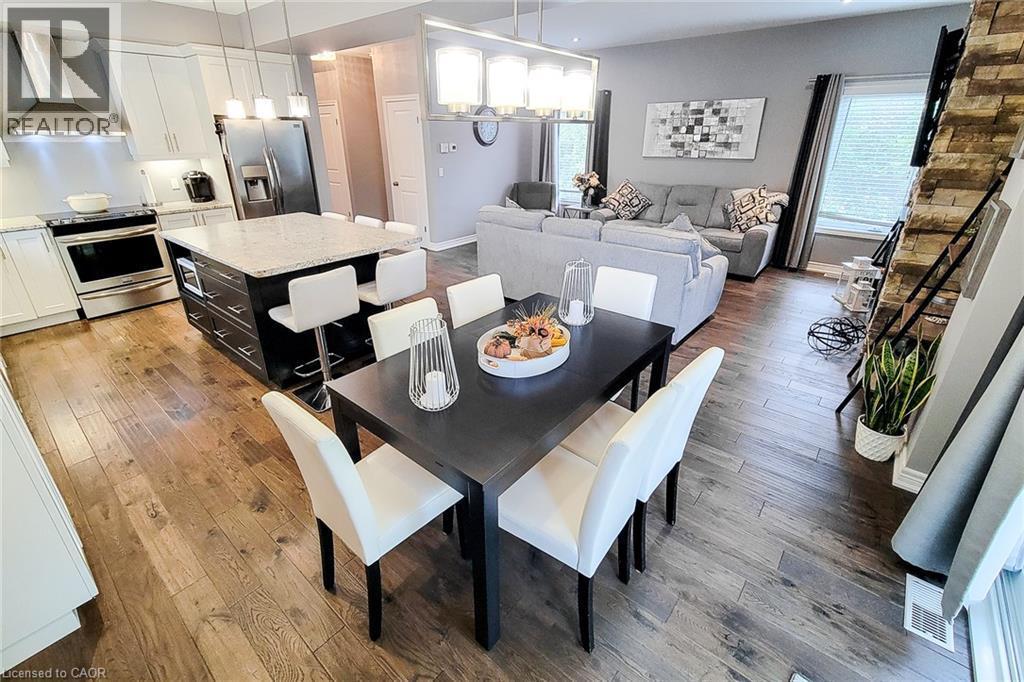 Open-concept main living area with wood-finish flooring, a kitchen island with seating, stainless steel appliances, a stacked stone accent wall, and recessed lighting - 4274 Sixth Avenue, Niagara Falls, ON
