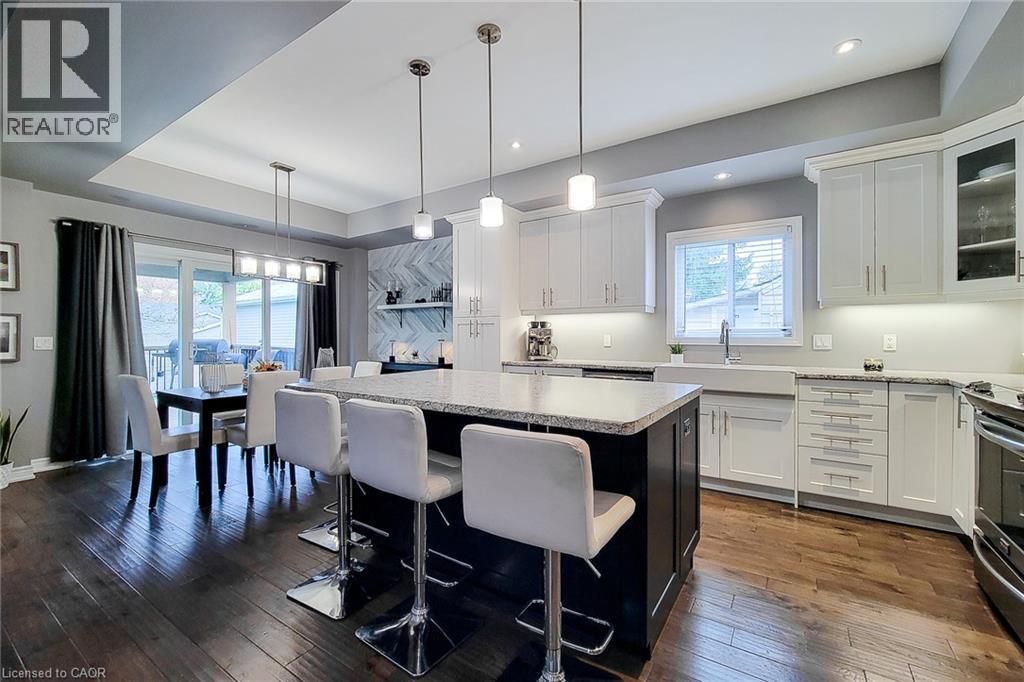 Kitchen featuring a center island with bar seating, white perimeter cabinetry, stone countertops, and a farmhouse-style sink - 4274 Sixth Avenue, Niagara Falls, ON