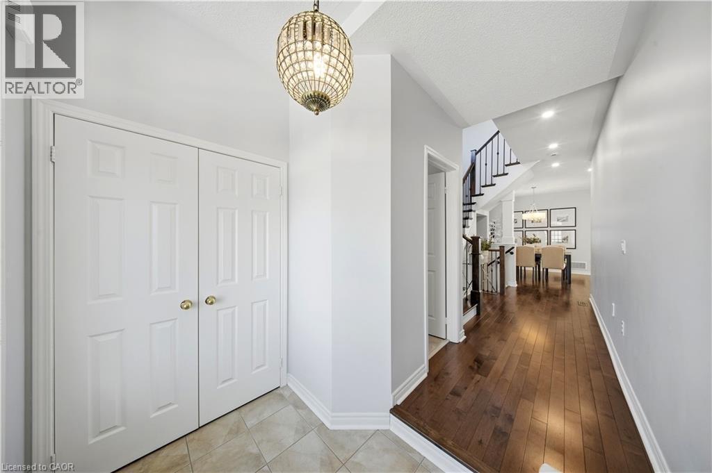 Recessed lighting, wood-finish flooring, staircase with dark wood railings, paneled bi-fold doors, and a decorative pendant light fixture - 3352 Hiscott Avenue, Burlington, ON