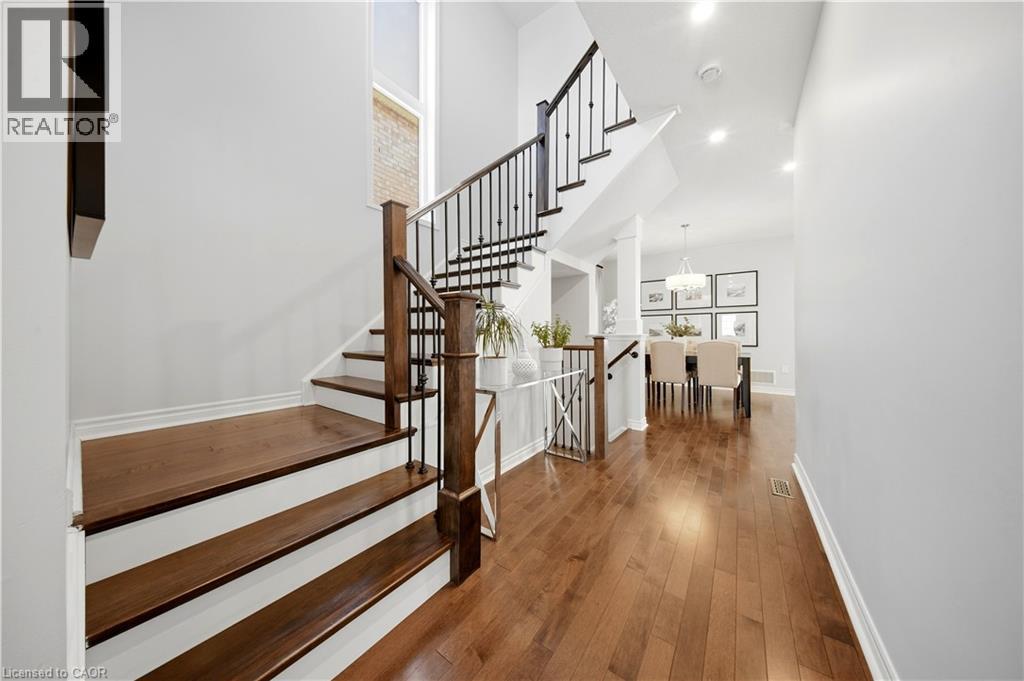 Hardwood flooring, wood-finish stairs with white risers, wrought iron and wood railings, recessed lighting, and a chandelier in the background - 3352 Hiscott Avenue, Burlington, ON