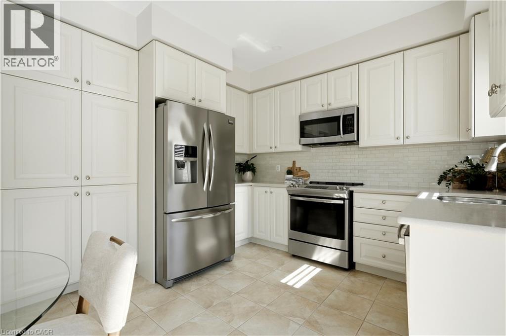 Kitchen featuring white cabinetry, stainless steel appliances, subway tile backsplash, and light-toned tile flooring - 3352 Hiscott Avenue, Burlington, ON