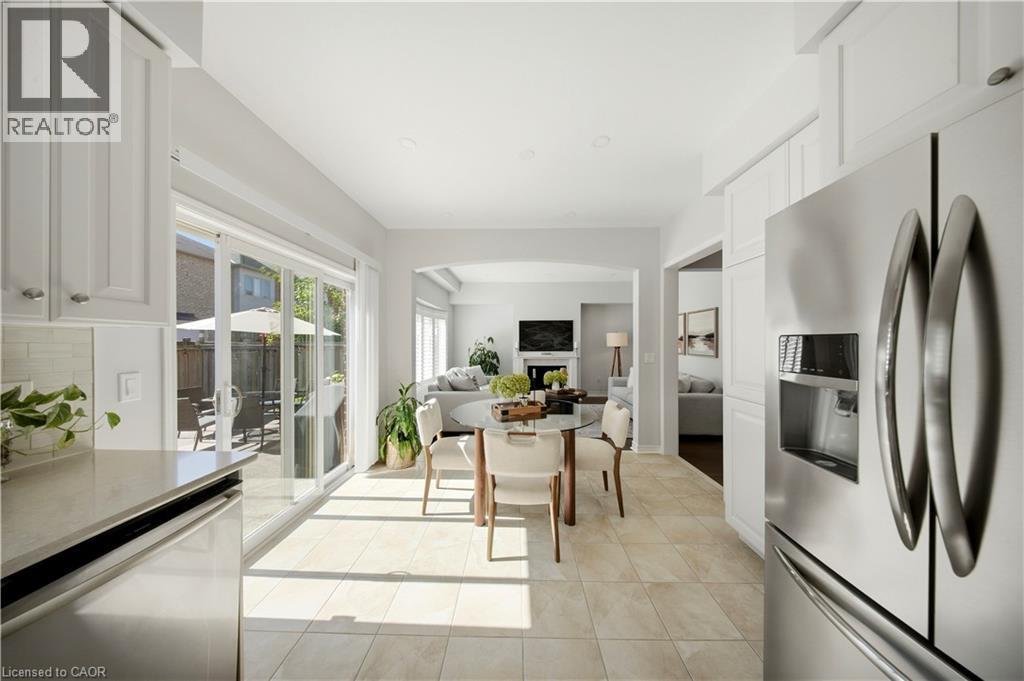 Stainless steel refrigerator, white shaker-style cabinetry, light-toned tile flooring, light-toned countertop, and sliding glass patio doors - 3352 Hiscott Avenue, Burlington, ON