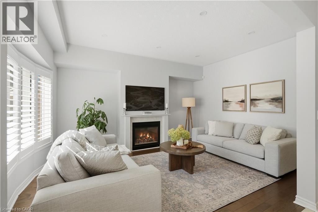 Living area featuring wood-finish flooring, a fireplace with a white mantel, and a bay window with white plantation shutters - 3352 Hiscott Avenue, Burlington, ON