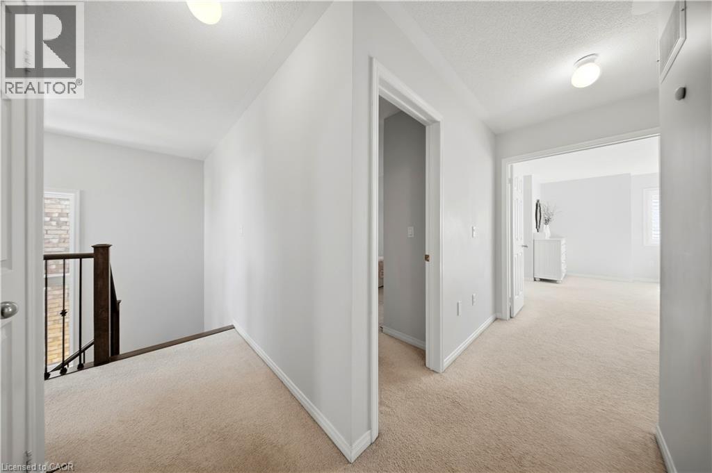 Carpeted hallway with white walls, recessed lighting, and a dark wood and iron stair railing - 3352 Hiscott Avenue, Burlington, ON