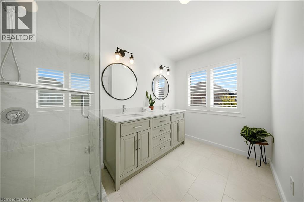 Spacious bathroom featuring a glass-enclosed shower, dual vanity with undermount sinks, and windows with louvered shutters - 3352 Hiscott Avenue, Burlington, ON