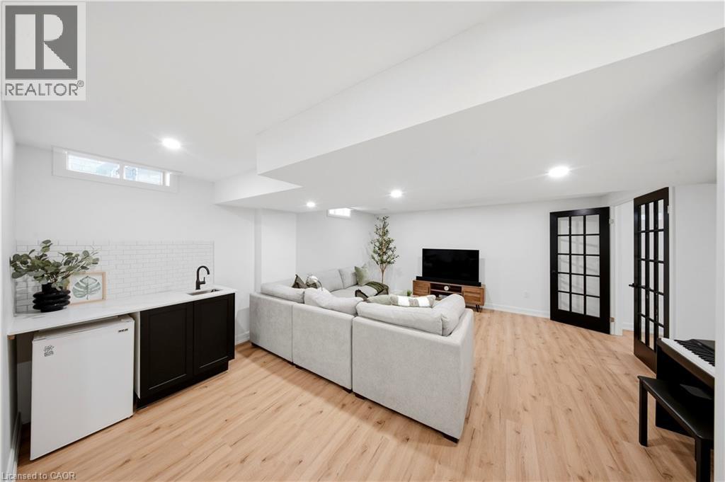 Spacious entertainment area featuring wood-finish flooring, recessed lighting, and a built-in wet bar with white subway tile backsplash and a black sink - 3352 Hiscott Avenue, Burlington, ON