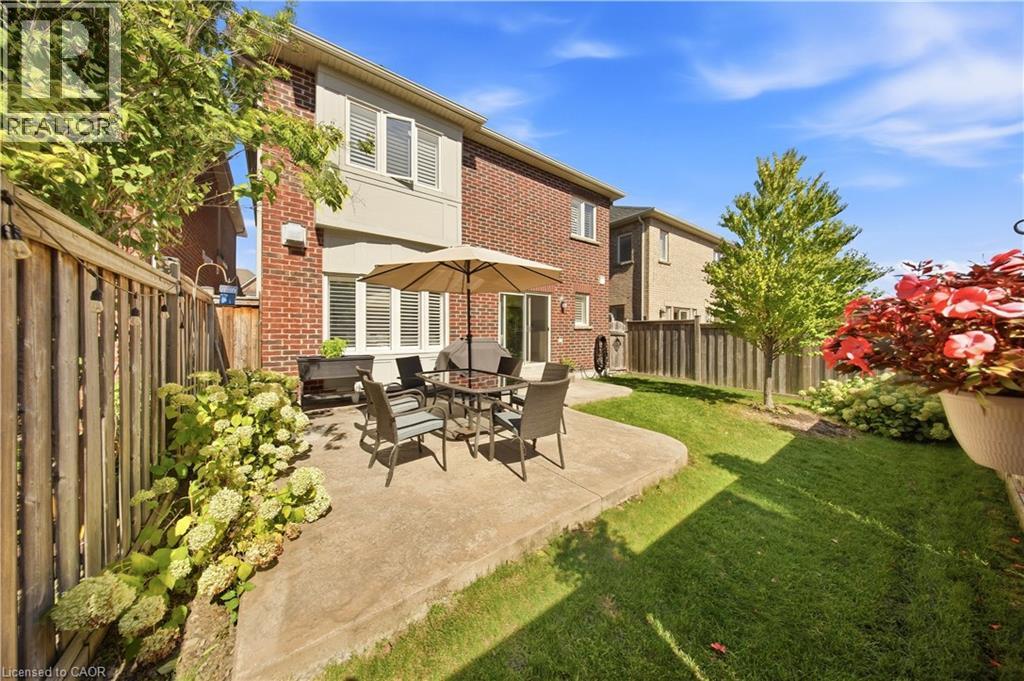 Expansive backyard featuring a concrete patio, manicured lawn, and mature trees - 3352 Hiscott Avenue, Burlington, ON
