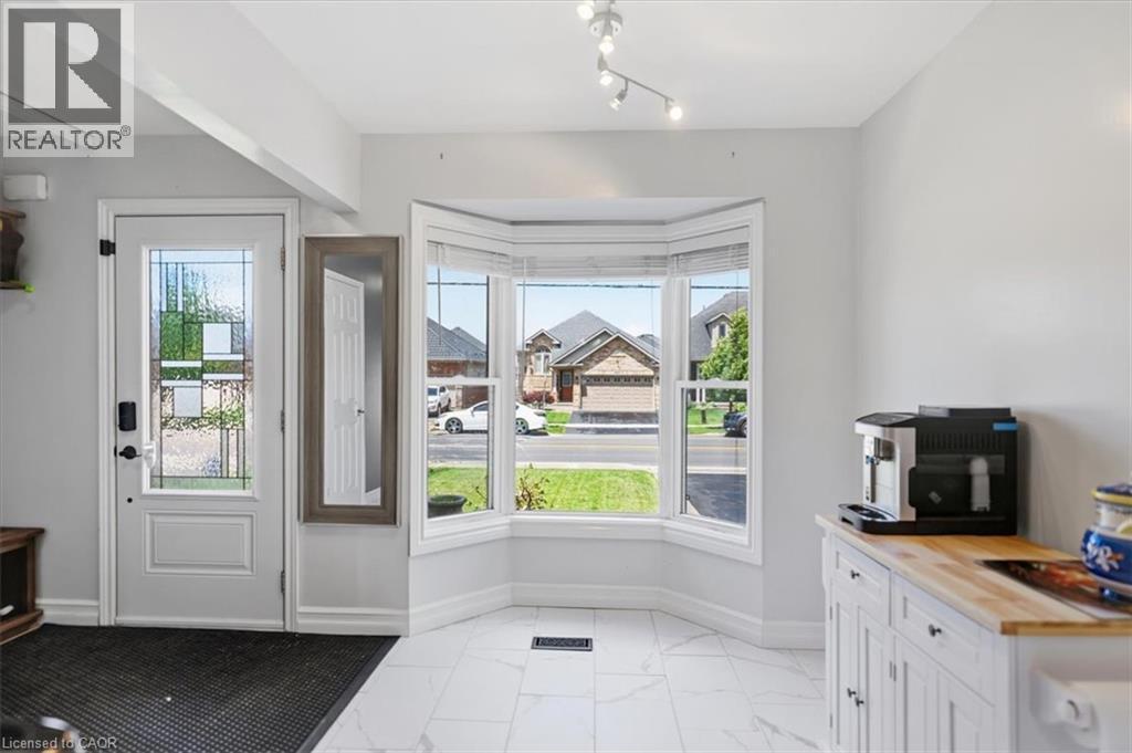 White entry door with decorative glass inserts, bay window with multiple panes, white tile flooring, and track lighting - 4804 John Street, Beamsville, ON