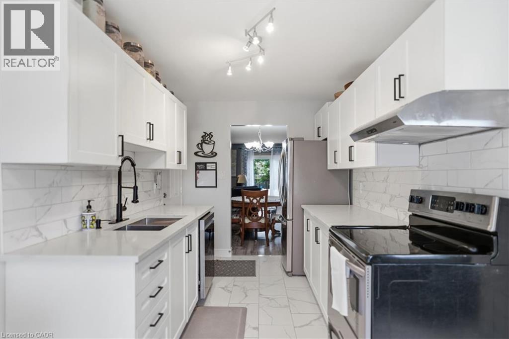 White shaker-style cabinetry with black hardware, stainless steel appliances, a subway tile backsplash, and a double basin sink with a matte black gooseneck faucet - 4804 John Street, Beamsville, ON