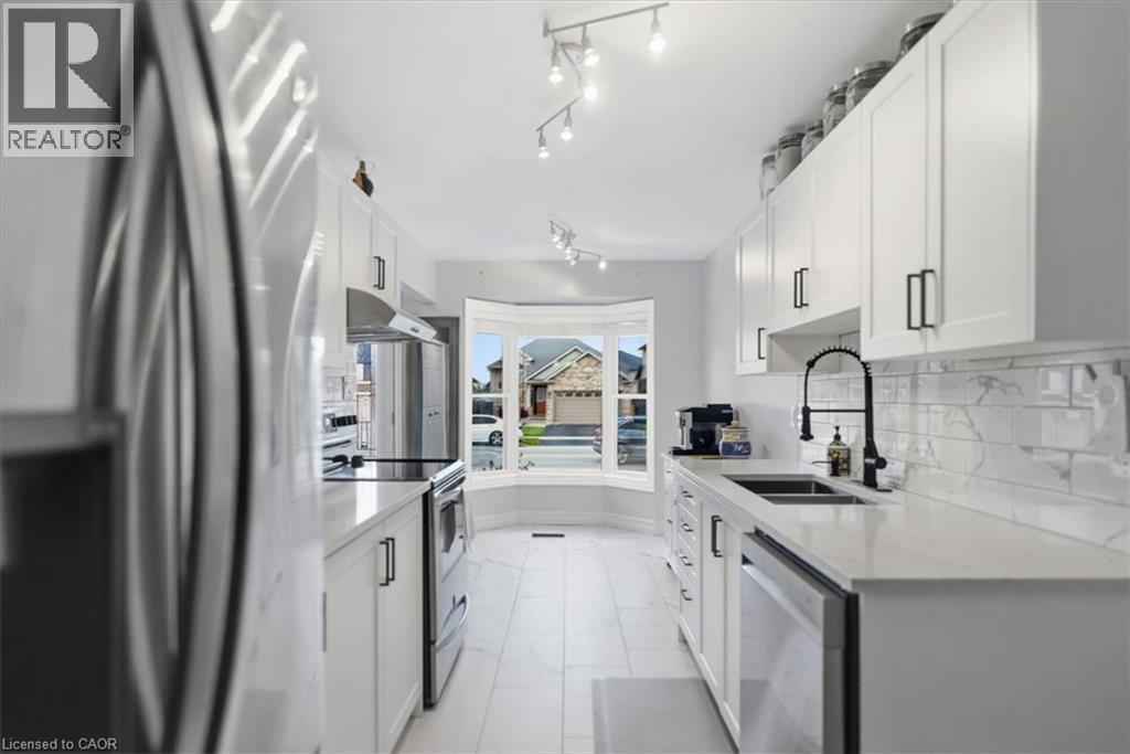 White cabinetry with black hardware, stainless steel appliances, marble-look subway tile backsplash, white countertops, and bay window - 4804 John Street, Beamsville, ON