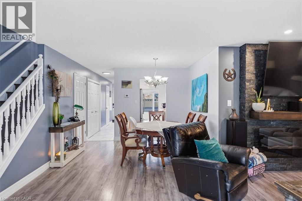 Wood-finish flooring throughout, white baluster staircase, stone-clad fireplace with mantel, recessed lighting, and a multi-arm chandelier - 4804 John Street, Beamsville, ON