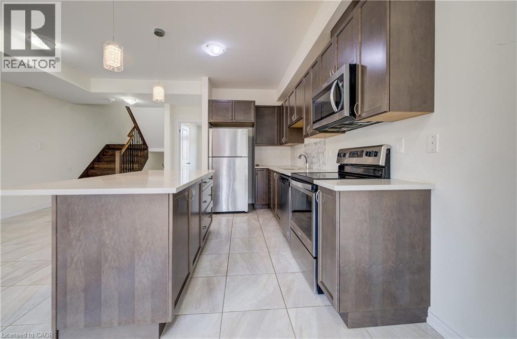 Kitchen featuring a center island with a light-toned countertop, stainless steel appliances, dark wood-finish cabinetry, tile flooring, and integrated lighting - 403 Westwood Drive Unit# 59, Kitchener, ON
