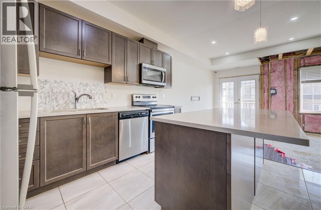 Kitchen featuring dark wood-finish cabinetry, stainless steel appliances, a white tile backsplash, and a light-toned countertop island - 403 Westwood Drive Unit# 59, Kitchener, ON