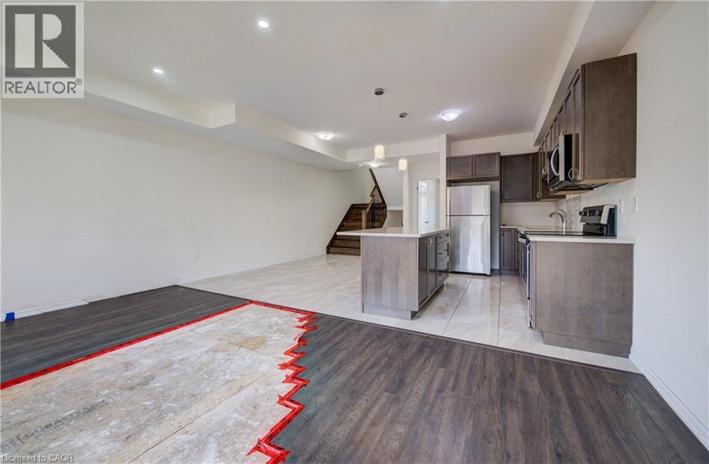 Kitchen featuring a central island with a light-colored countertop, dark wood-finish cabinetry, stainless steel appliances, and light-colored tile flooring - 403 Westwood Drive Unit# 59, Kitchener, ON