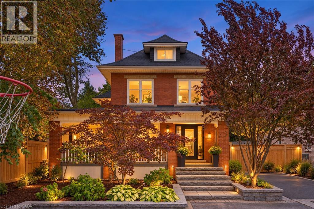 Brick exterior with a prominent front entrance, featuring a covered porch with white railing, and a gabled dormer - 283 Plains Road W, Burlington, ON