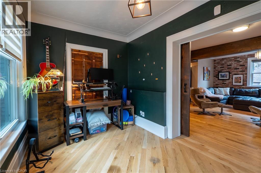 Hardwood flooring throughout, with a dark green wall finish, white trim, and a sliding barn door - 283 Plains Road W, Burlington, ON