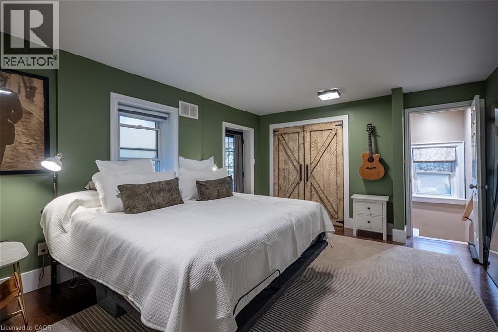 Rich olive-toned walls, wood-finish flooring, two windows with white trim, a barn door style closet, and white overhead lighting - 283 Plains Road W, Burlington, ON