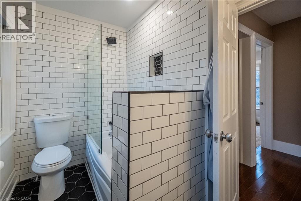 Bathroom featuring subway tile walls, black hexagonal floor tiles, a built-in shower niche, and a glass shower partition - 283 Plains Road W, Burlington, ON