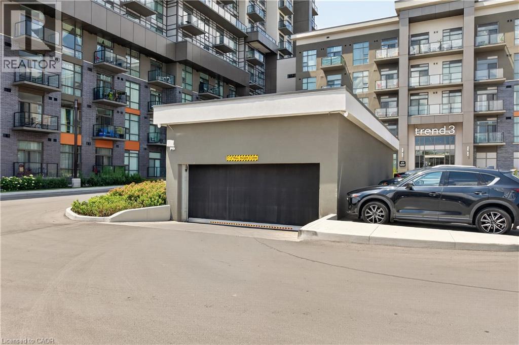 Underground parking entrance featuring a roll-up door, adjacent to modern multi-story buildings with balconies - 10 Mallard Trail Unit# 237, Waterdown, ON