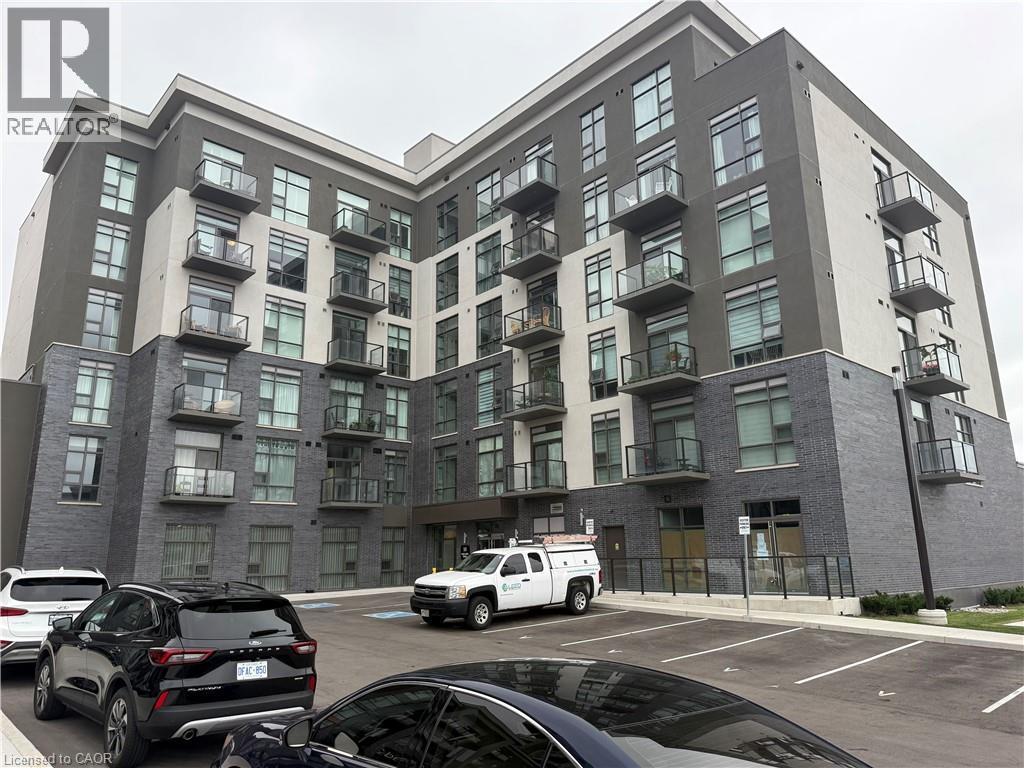Modern multi-story building featuring a facade of grey brick and light-colored panels, private balconies with glass railings, and a dedicated surface parking area - 10 Mallard Trail Unit# 237, Waterdown, ON