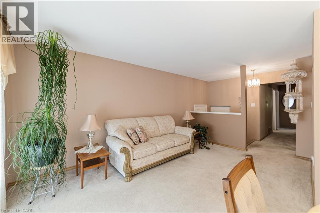 Carpeted living area with neutral wall tones, a partial wall separation, and a chandelier fixture - 450 Brigadoon Drive, Hamilton, ON