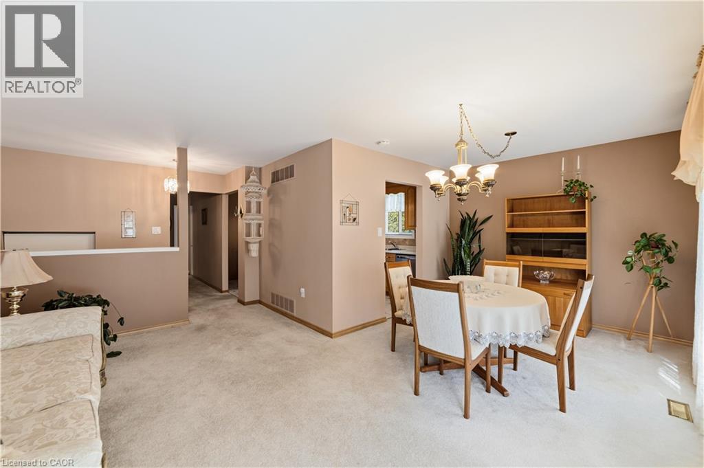 Open-concept living and dining area featuring neutral carpeting, a brass-finish chandelier, and a half-wall partition - 450 Brigadoon Drive, Hamilton, ON