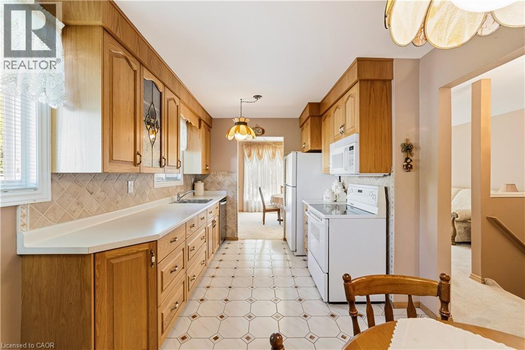 Galley kitchen featuring wood cabinetry, light countertops, a tiled backsplash, and patterned tile flooring - 450 Brigadoon Drive, Hamilton, ON