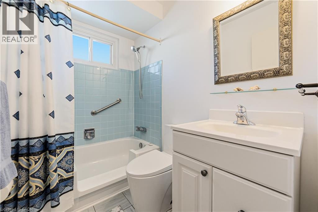 Bathroom featuring a white vanity with integrated sink, an ornate framed mirror, a glass display shelf, light blue square wall tiling (original still in great shape), and a white bathtub modified for - 450 Brigadoon Drive, Hamilton, ON