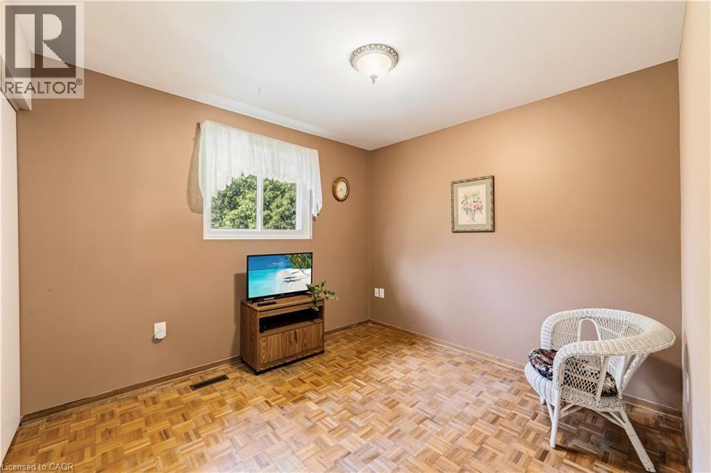 Bedroom, can be used as a TV room or office. Featuring neutral-toned walls, a white-framed window with natural light, closet and wood-finish parquet flooring - 450 Brigadoon Drive, Hamilton, ON