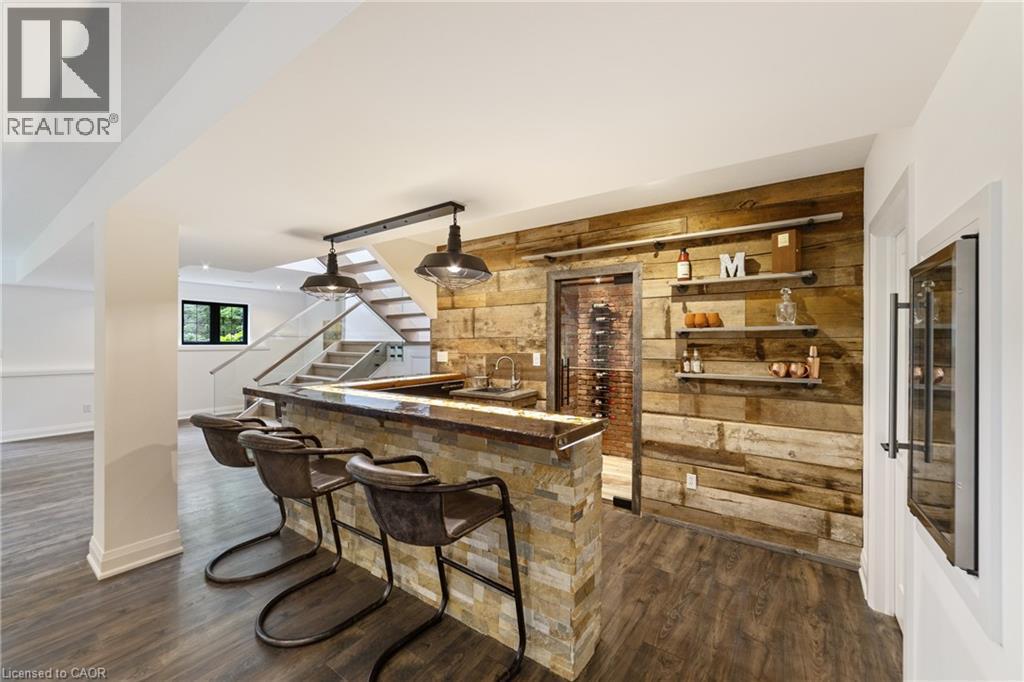Wet bar with custom countertop with built in lighting, seating for 5+, rustic overhead lights, barn board wall with shelving and bar fridge - 515 Hamilton Drive, Ancaster, ON