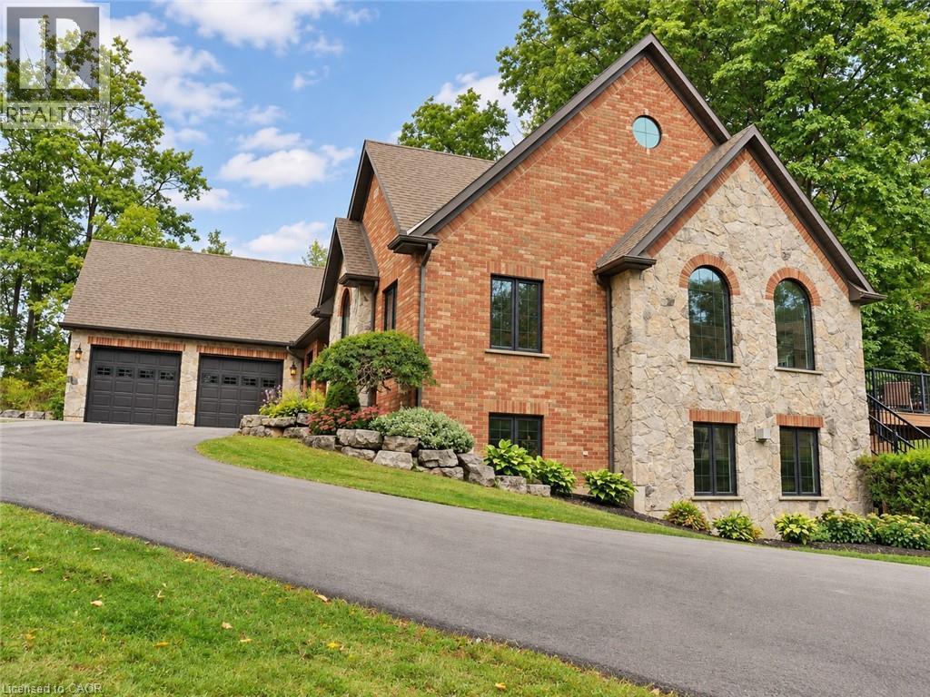 Stone and brick exterior with arched windows, a circular window, and a paved driveway leading to a two-car garage and guest house on property - 515 Hamilton Drive, Ancaster, ON