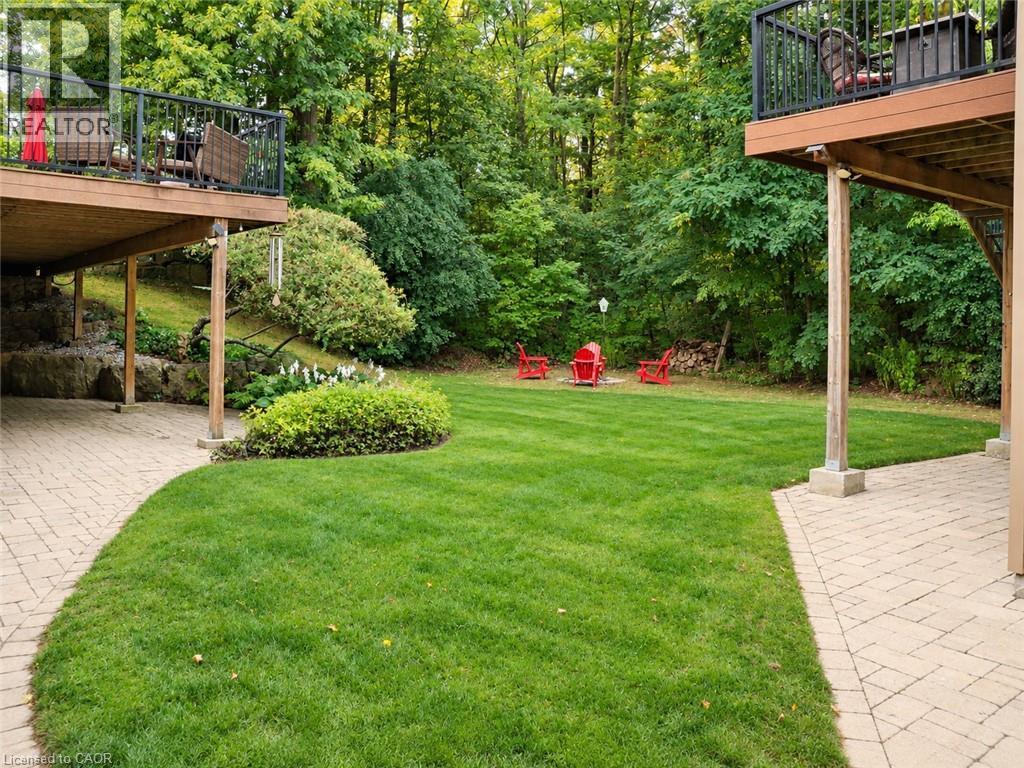 Expansive backyard featuring a manicured lawn, two elevated wood decks with black railings, and a stone paver patio - 515 Hamilton Drive, Ancaster, ON